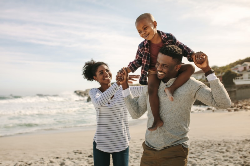 happy family walking on beach with young son on dad's shoulders